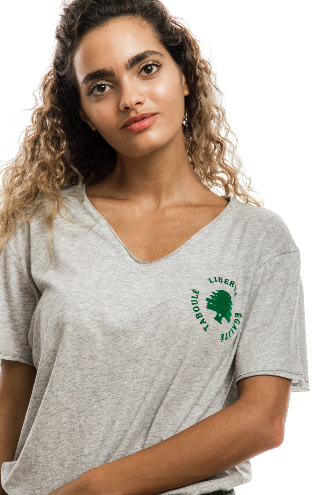 young adult female wearing grey t-shirt with liberté égalité taboulé written in french and in green in the center of the t-shirt along with olive green shorts