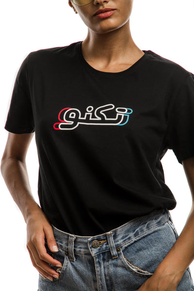 young adult female wearing black t-shirt with techno written in arabic تكنو and in blue, red and white in the center of the t-shirt along with blue jeans shorts