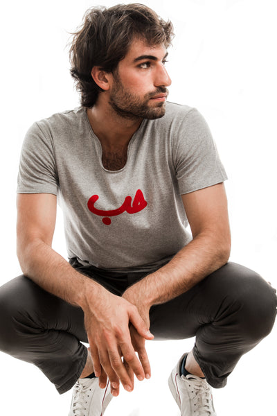 young adult male wearing grey t-shirt with Hobb written in arabic حب and in red velvet in the center of the t-shirt along with black pants