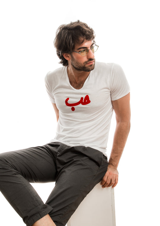 young adult male wearing white t-shirt with Hobb written in arabic حب and in red velvet in the center of the t-shirt along with black pants and glasses