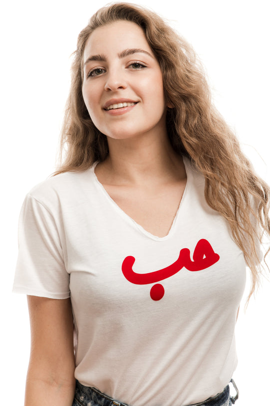 young adult female wearing white t-shirt with Hobb written in arabic حب and in red velvet in the center of the t-shirt along with blue jeans shorts