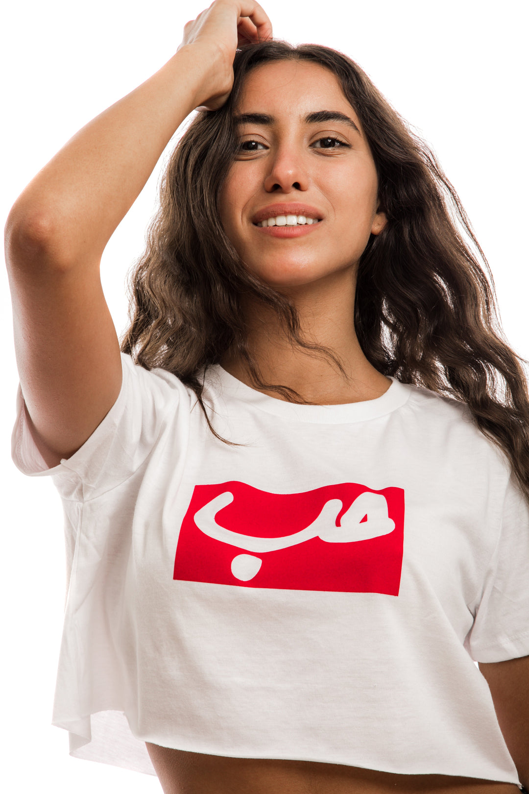 young adult female wearing white crop top with hobb written in arabic حب in white and in a red frame in the center of the crop top