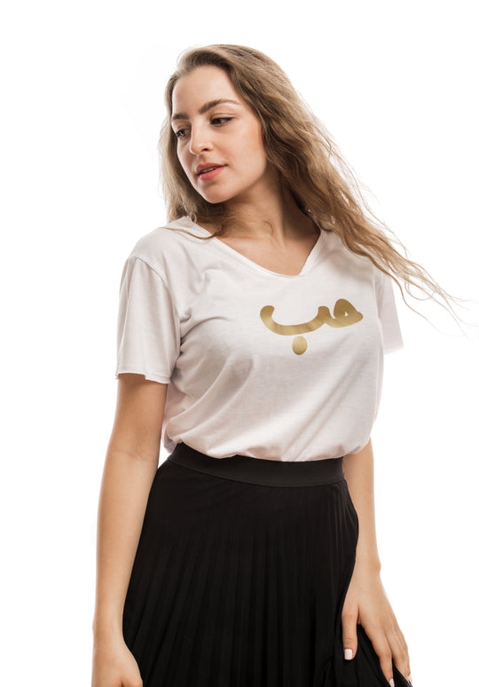 young adult female wearing white t-shirt with hobb written in arabic حب and in gold in the center of the t-shirt along a black skirt