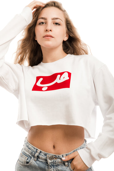 young adult female wearing white crop sweater with hobb written in arabic حب in white and in a red frame in the center of the crop sweater along with teared jeans
