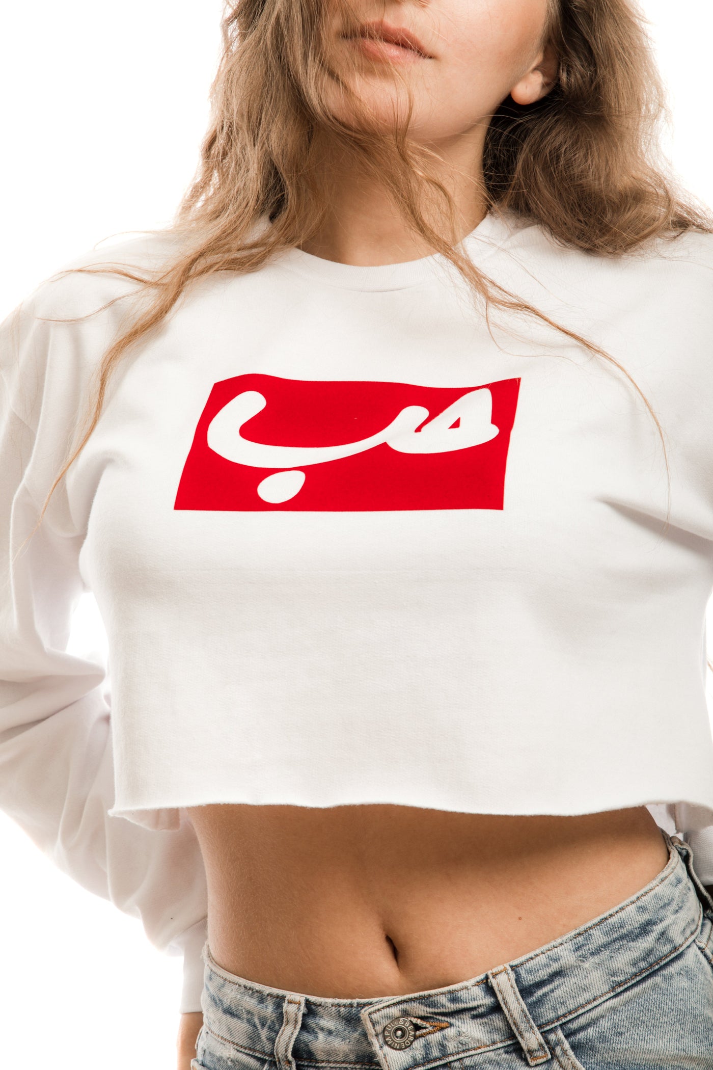 young adult female wearing white crop sweater with hobb written in arabic حب in white and in a red frame in the center of the crop sweater along with jeans