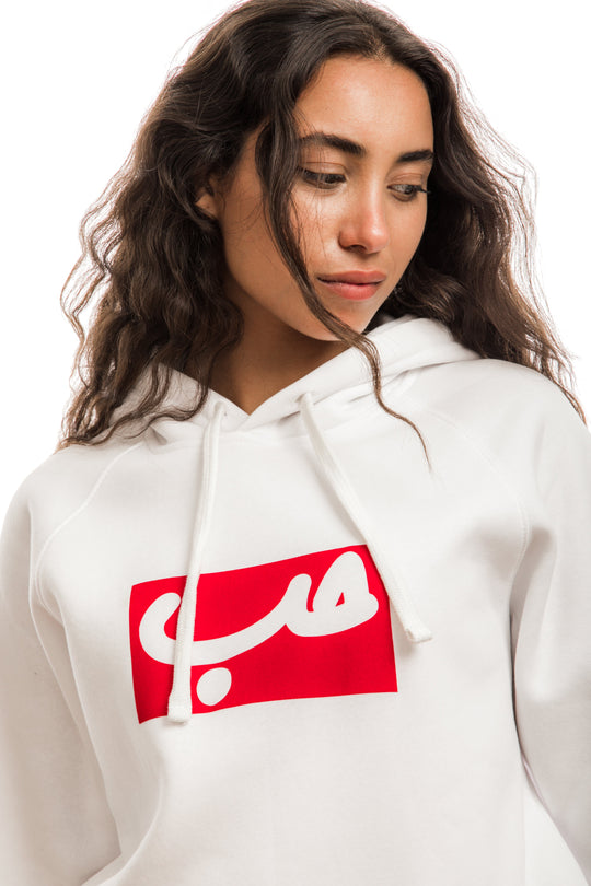 young adult female wearing white hoodie with hobb written in arabic حب in white and in a red frame in the center of the hoodie