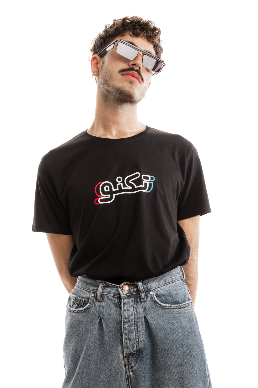 young adult male wearing black t-shirt with techno written in arabic تكنو and in blue, red and white in the center of the t-shirt along with blue jeans and sunglasses